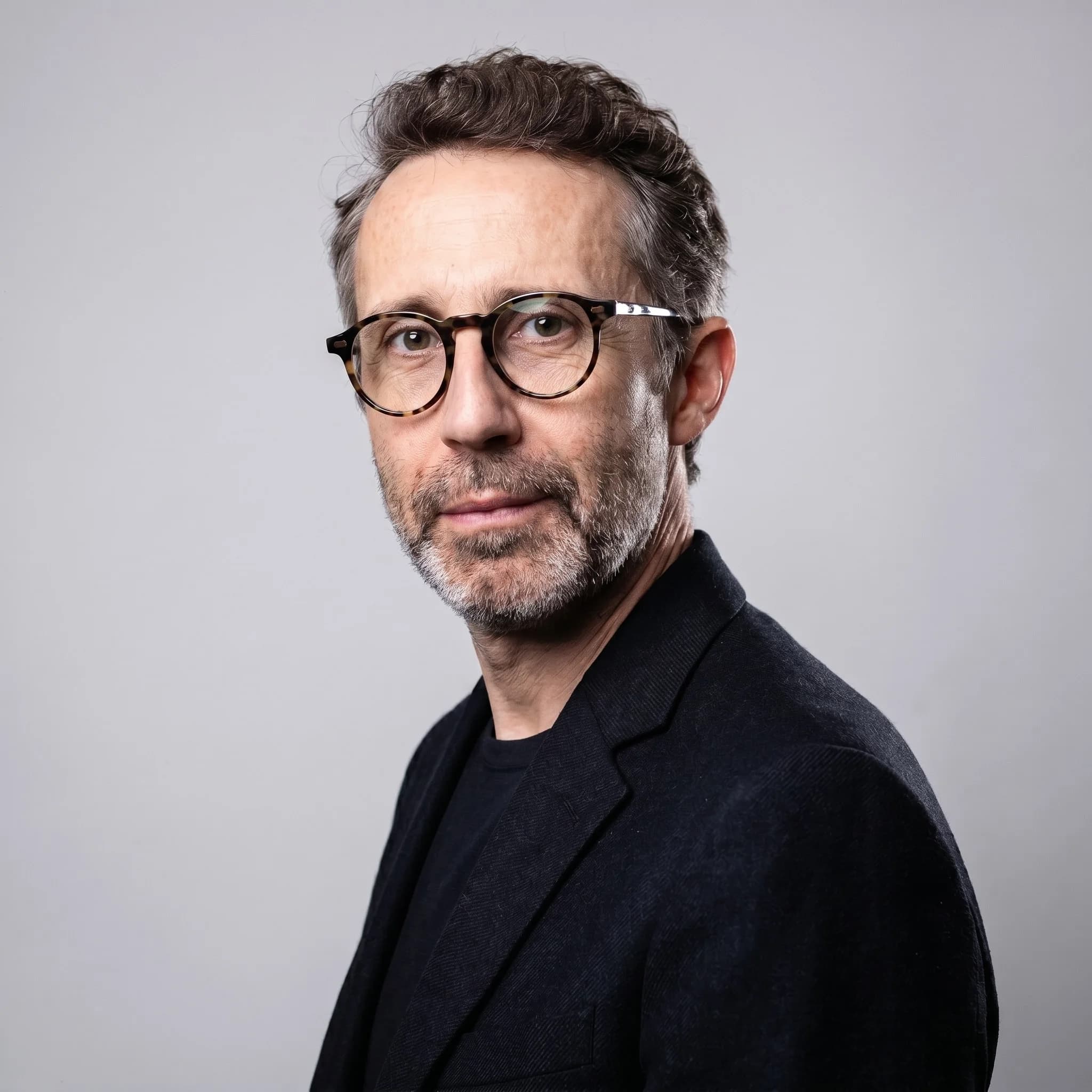 Portrait corporate dirigé en IA : homme en veste noire sur fond gris clair uni, de trois-quarts, regard posé vers l'objectif.